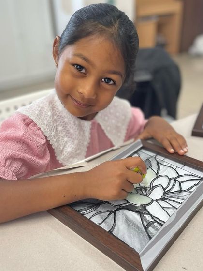 A young girl smiles as she works on her glass painting project, carefully filling in the design with vibrant colors.