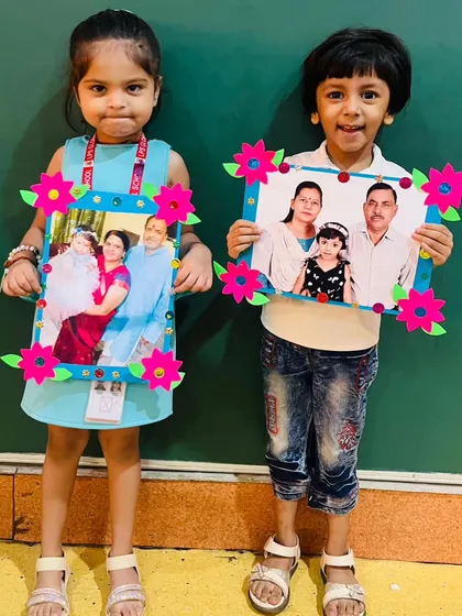 Two young girls display their decorated photo frames, each holding a cherished family picture.
