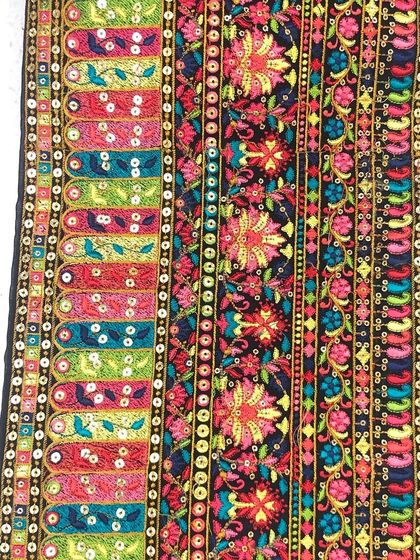 This vibrant, multi-colored embroidered border showcases a mix of floral and geometric patterns with sequin accents. It's a perfect example of a festive trim for lehengas and Garba outfits.