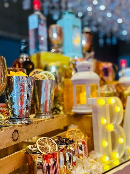 A close-up of the Gatsby bar's glowing details. The lit-up 'BAR' sign reflects on the mirrored surface, surrounded by ornate gold and copper glassware filled with aromatic garnishes like dried orange slices.