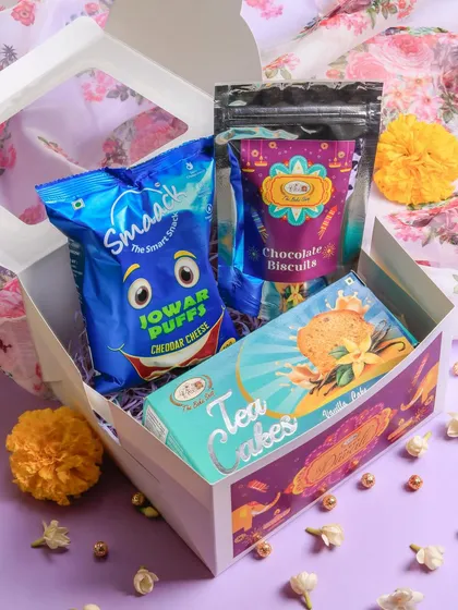 The 'Brightness Box' is a delightful mix of sweet and savory. This Diwali hamper includes a Vanilla Tea Cake, Chocolate Biscuits, and a pack of savory Jowar Puffs.