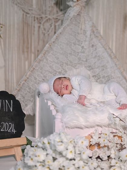 A smiling newborn in an all-white boho setup, complete with a personalized chalkboard.