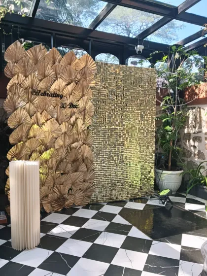 A highly modern and artistic backdrop. This piece combines a wall of gold dried palm leaves with a textured gold sequin panel for a unique and glamorous photo opportunity.