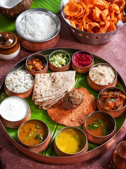 A traditional South Indian thali served in a large copper plate with numerous small bowls. This top-down shot showcases the variety and balance of flavors in a complete meal from Bengaluru.