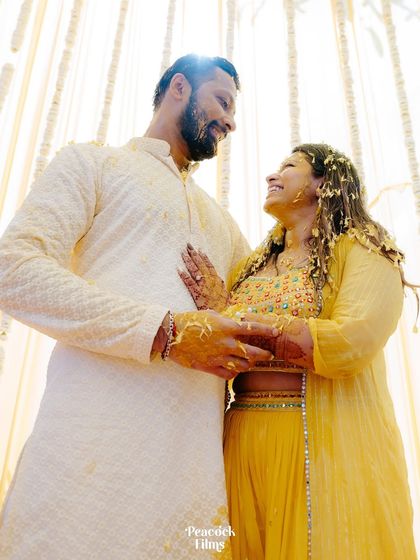 A low-angle shot of the couple during their Haldi ceremony, their faces glowing with happiness and covered in turmeric.