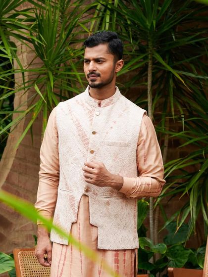 Adjusting the cuff on a peach-colored kurta and printed vest, a simple gesture that adds a touch of authenticity to the photograph.