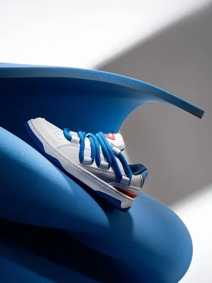 A single white sneaker nestled in a curved blue foam sheet. This abstract setup highlights the shoe's design and colors in a creative and visually interesting way.