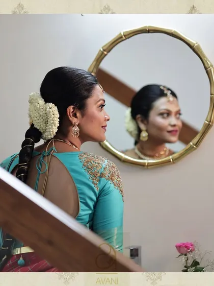 A bride looking in the mirror, revealing the elegant back design of her turquoise blouse. The piece features a simple tie-up detail and delicate embroidery, showcasing a subtle and graceful style.