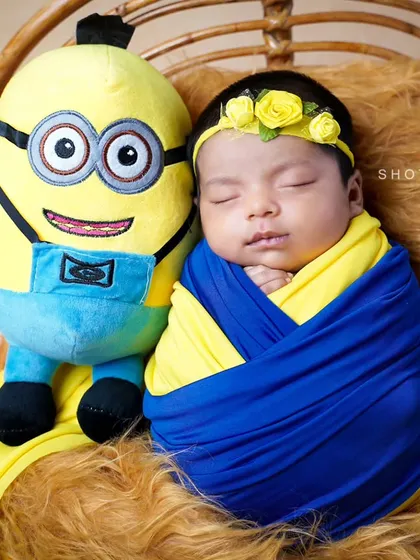 One in a minion. This adorable newborn is wrapped in yellow and blue, sleeping soundly next to his favorite cartoon character during a themed shoot at home.