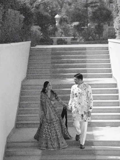 A timeless black and white shot of the couple descending a grand staircase. This classic pre-wedding photograph emphasizes the elegance of their traditional attire and the grandeur of the location.