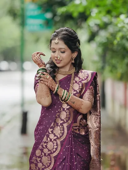 The bride adjusting her bangles, a classic pose that shows off her intricate henna and the rich fabric of her purple engagement saree.