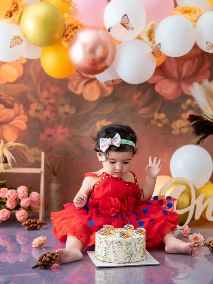 This little girl is about to dig into her first birthday cake, surrounded by a beautiful autumn-themed balloon and floral arrangement.