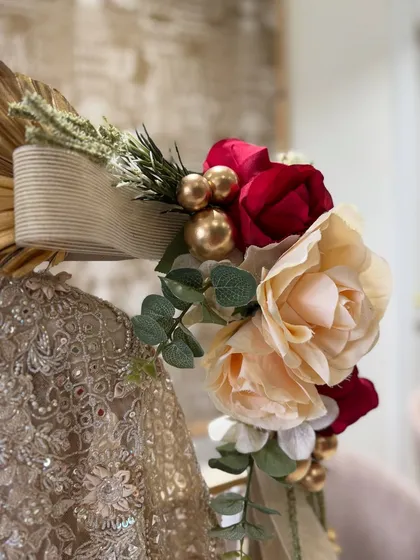The delicate art of adornment. A close-up of the hand-tied floral arrangement on an ivory trousseau piece, featuring soft roses and gold accents.