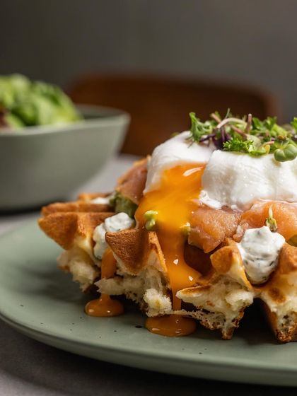 A close-up of the poached egg on our Smoked Salmon Waffle, its golden yolk cascading over the delicate salmon and waffle.
