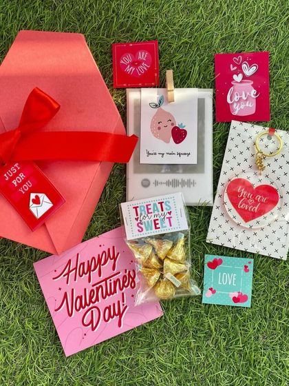 A sweet Valentine's Day gift set laid out on the grass. It includes a custom Spotify plaque, Hershey's Kisses, and adorable love-themed cards.