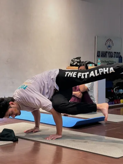 A student holds Astavakrasana (Eight-Angle Pose), a complex arm balance that strengthens the entire body.