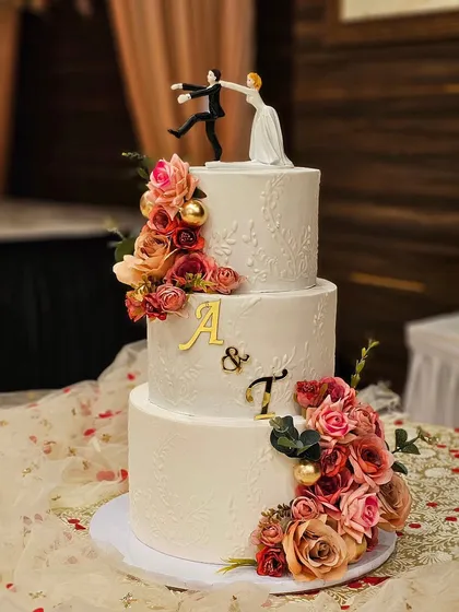 A classic three-tier white wedding cake with a cascade of rustic pink flowers and a fun, quirky bride-and-groom topper.