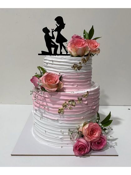 A beautiful 3kg two-tier engagement cake. The design features a pink and white ombre effect with textured frosting, gold leaf accents, and fresh roses.