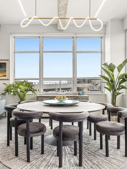 In the heart of this New York Apartment, a pedestal dining table is surrounded by light, moveable chairs, perfect for gatherings. The layout is designed to maximize space and enhance the stunning view of the Brooklyn skyline.