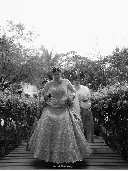 A classic black and white shot of the bride's entrance, her grand lehenga filling the frame as she walks across a bridge.