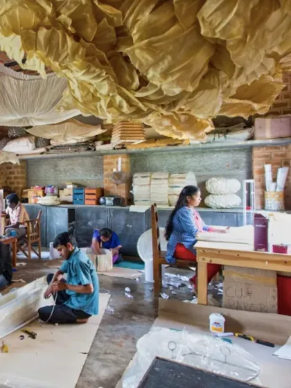 The interior of the Oorjasi paper-making workshop. The space is a hive of activity, with high ceilings and large windows providing ample light for the artisans at work. The exposed brick walls add to the studio's rustic, creative character.
