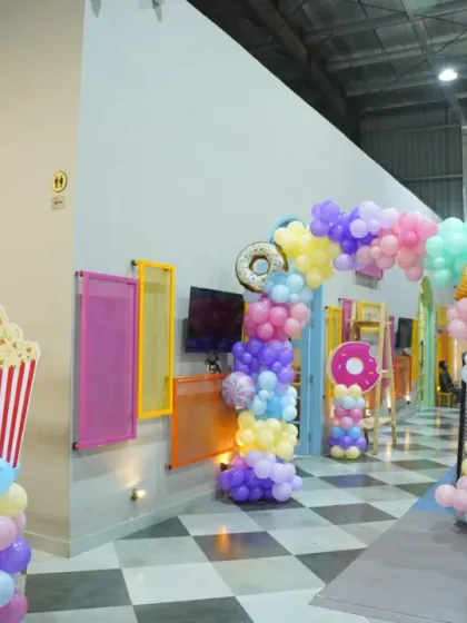 A whimsical candy and donut-themed balloon arch welcomes guests to the play area. The creative popcorn prop adds a fun, unique touch to the decor.