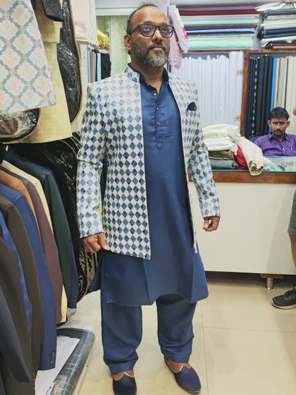 A client wearing the blue and white diamond-patterned open shrug over a Pathani suit, seen from the front.