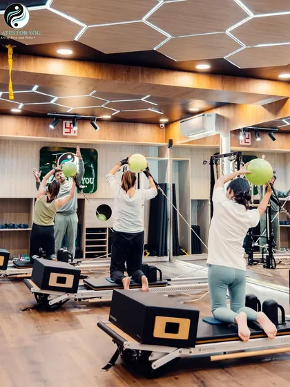 A group of clients uses stability balls on the reformer to challenge their balance and engage their core muscles more deeply during this kneeling exercise.