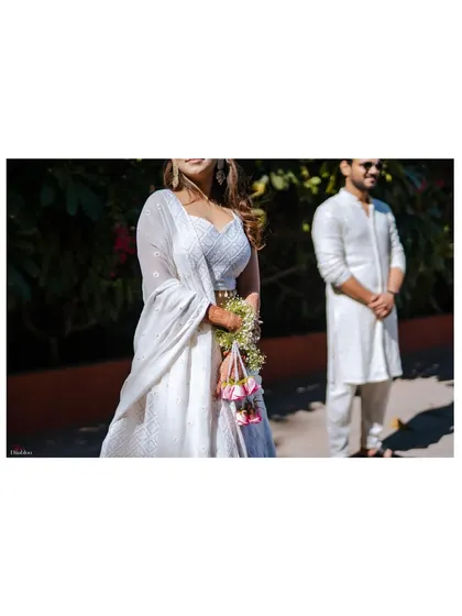 A detail shot focusing on the bride's beautiful white lehenga and floral kaleeras. We believe in capturing all the elements that make your look special and unique.