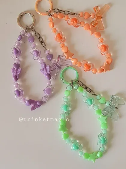 The full set of pastel beaded keychains in purple, orange, and green. Each one is a unique combination of hearts, stars, and a cute bow charm.