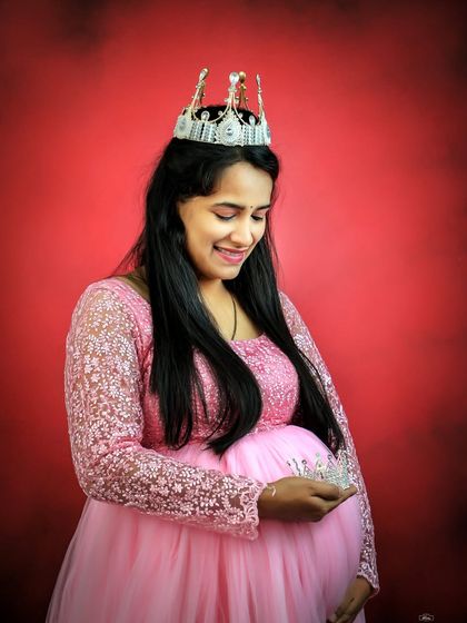 A sweet and symbolic portrait of a mother-to-be in a pink gown. She holds a small crown over her baby bump, signifying the little prince or princess on the way.