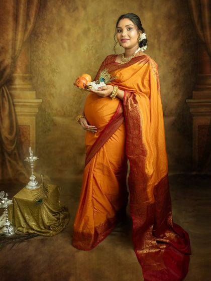 Embracing tradition with a beautiful orange silk saree. Holding a platter of fruits and flowers, this portrait is rich with cultural symbolism, celebrating the life you are growing.