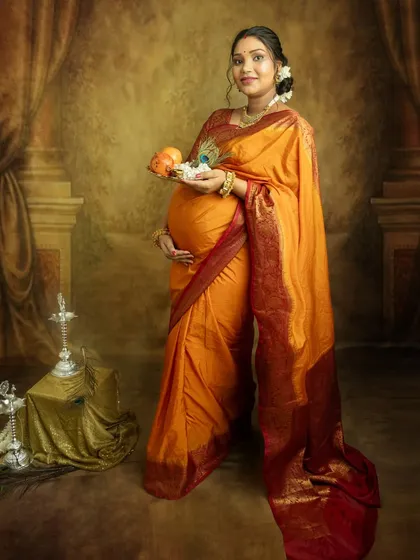 Embracing tradition with a beautiful orange silk saree. Holding a platter of fruits and flowers, this portrait is rich with cultural symbolism, celebrating the life you are growing.