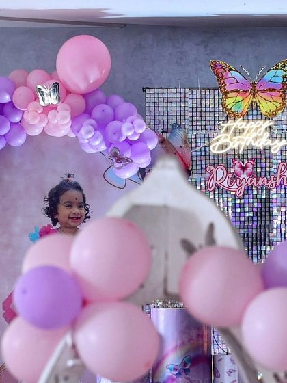 A candid shot of the birthday girl enjoying her butterfly-themed party. The background shows the shimmer wall and neon sign, creating a magical atmosphere.