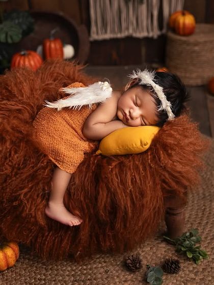 A little angel sleeping peacefully in an autumn-themed setting. The tiny angel wings add a touch of magic to the warm, rustic setup with pumpkins and pinecones.