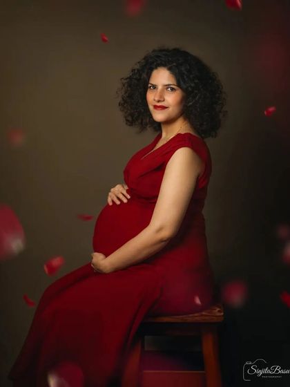 A duplicate of ID 6, an expecting mother in a vibrant red dress is showered with falling rose petals in this romantic studio portrait. The rich colors and dynamic elements create a feeling of celebration and love.