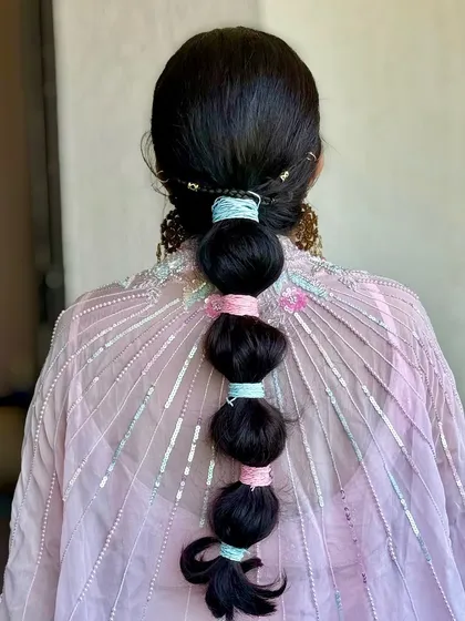 A playful and modern bubble braid, accented with pastel-coloured threads to match the client's outfit. This is a great hairstyle for a Mehendi or Sangeet.