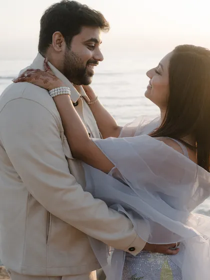 An embrace filled with smiles against the backdrop of the setting sun and sea. This candid engagement photo captures the easy, happy love between the couple.