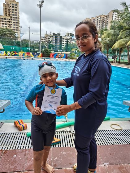 A female coach presents a certificate to a young boy, celebrating his advancement to a new skill level at our swim school.