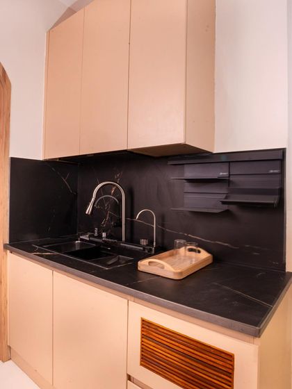 A minimalist pantry or wet kitchen area with a black marble backsplash and simple, handleless cabinetry.