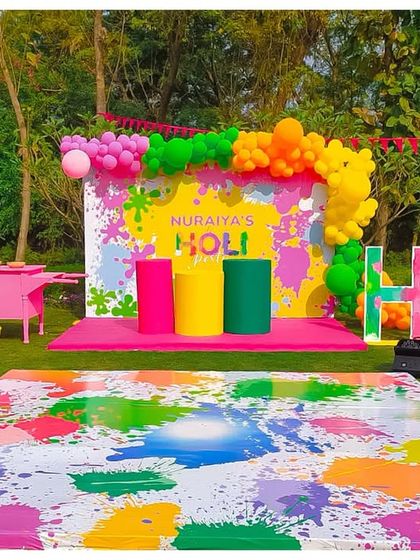 A colourful and fun setup for a Holi party. The backdrop is a splash of bright colours, with large 'HOLI' letters and a custom dance floor designed to look like it's covered in paint.