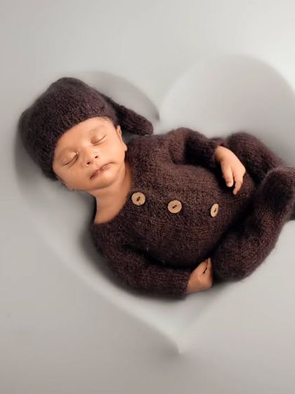 A minimalist and modern newborn portrait of a baby in a brown knit outfit, sleeping inside a heart-shaped white bowl.