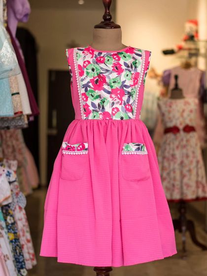 This bright pink dress features a beautiful floral panel on the bodice and matching trim on the pockets. It's a fun, practical, and stylish choice for any day.