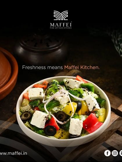 A bowl of our Greek Salad, made with fresh cucumbers, tomatoes, bell peppers, onions, and olives, topped with a generous block of feta cheese and a light vinaigrette.