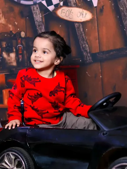 A toddler boy enjoys a ride in a toy car against a rustic garage-themed backdrop.
