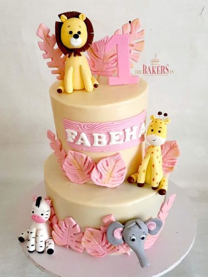 A pretty-in-pink jungle theme cake for Fabeha's first birthday. This two-tier design features cute, friendly jungle animals and pink tropical leaves for a softer take on the popular theme.