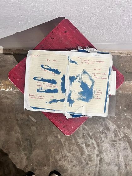A participant's experimental cyanotype on a ruled notebook page, combining a handprint with handwritten text. This shows the versatility of the process, allowing for deeply personal and mixed-media artistic expressions.