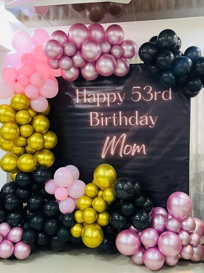 A chic backdrop for a 53rd birthday, using a black panel and a modern balloon arrangement in pink, gold, and black.