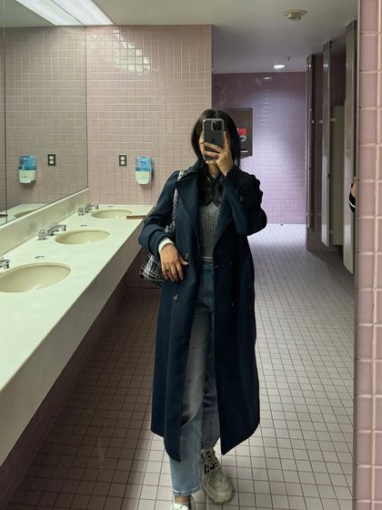 A mirror selfie showing a classic trench coat look, a staple for any college student's wardrobe.