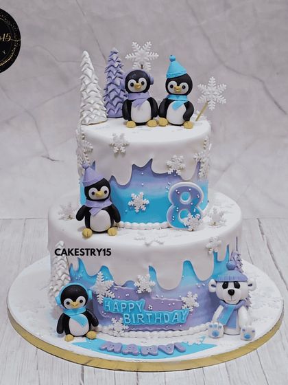 A fun 4kg two-tier penguin-themed cake for an eighth birthday. This chocolate cake is designed to look like a winter wonderland, with cute fondant penguins and a polar bear.